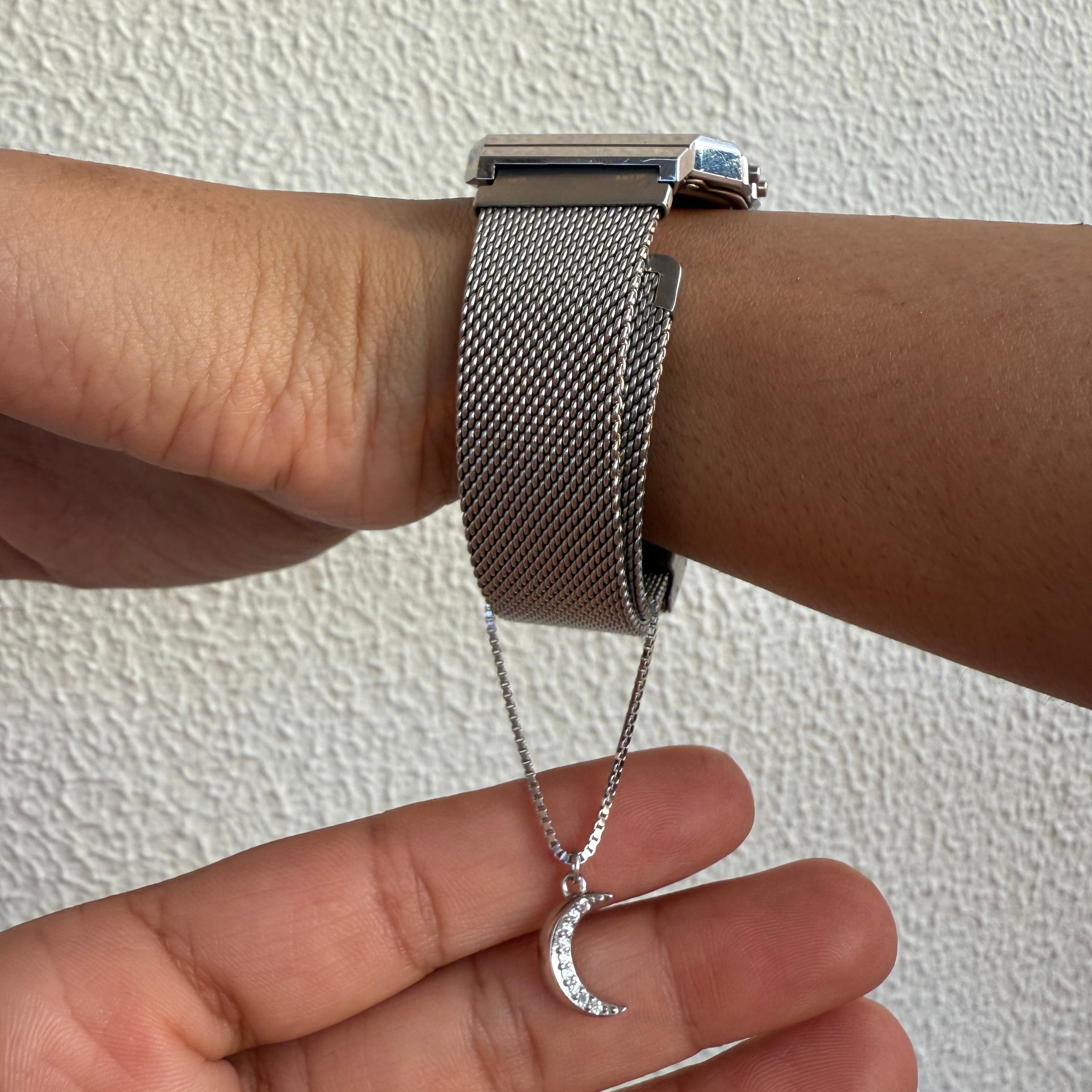 Silver watch on wrist with matching necklace featuring a moon pendant against a neutral background